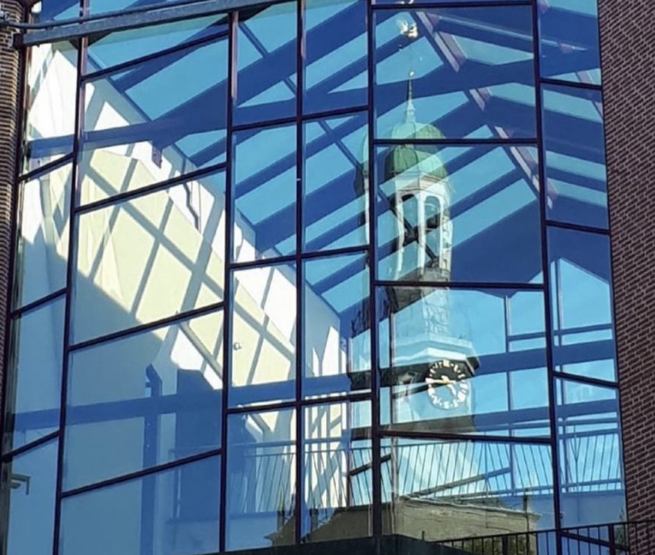 Doorkijkje bij de glazen entree van het stadskantoor met weerspiegeling van de kerktoren
